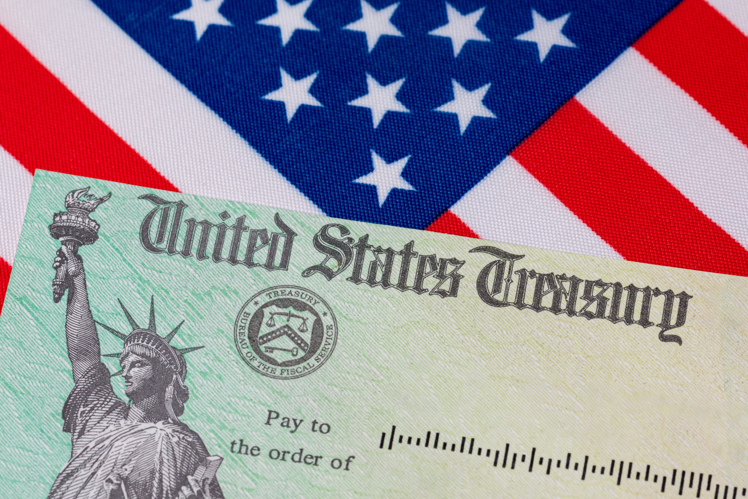 United States Treasury check and American flag. Concept of stimulus payment, tax refund. Federal government grants, loans, benefits and assistance