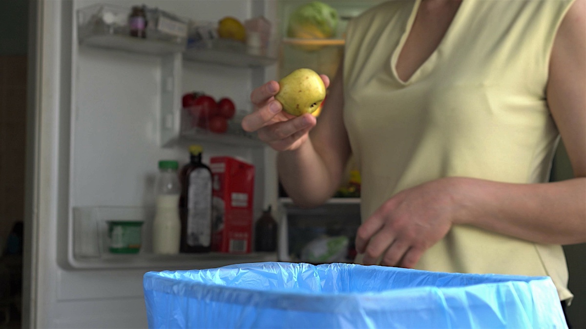 Throwing food waste in the trash. Household food loss. Food spoilage at home occurs due to improper storage. A woman throws uneaten expired fruits out of the refrigerator.