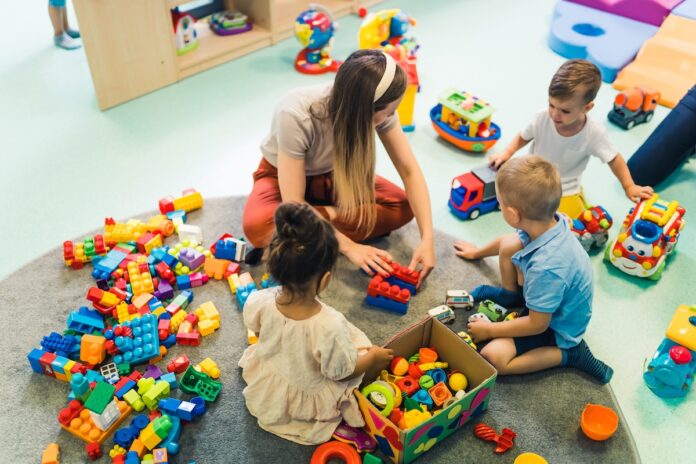 Playtime at nursery school. Toddlers with their teacher sitting on the floor and playing with building blocks, colorful cars and other toys.